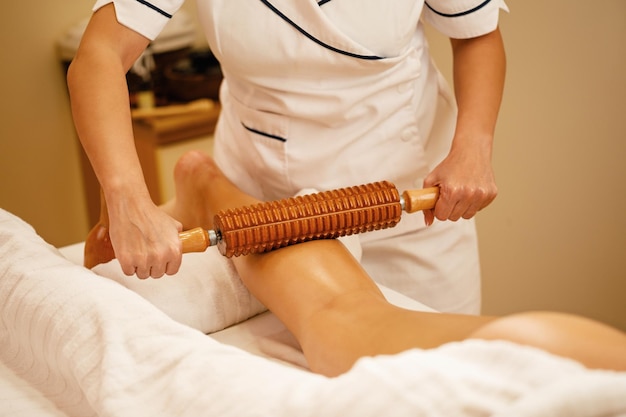 terapeuta-irreconocible-realizando-maderoterapia-piernas-mujer-tratamiento-masaje-spa_637285-2126
